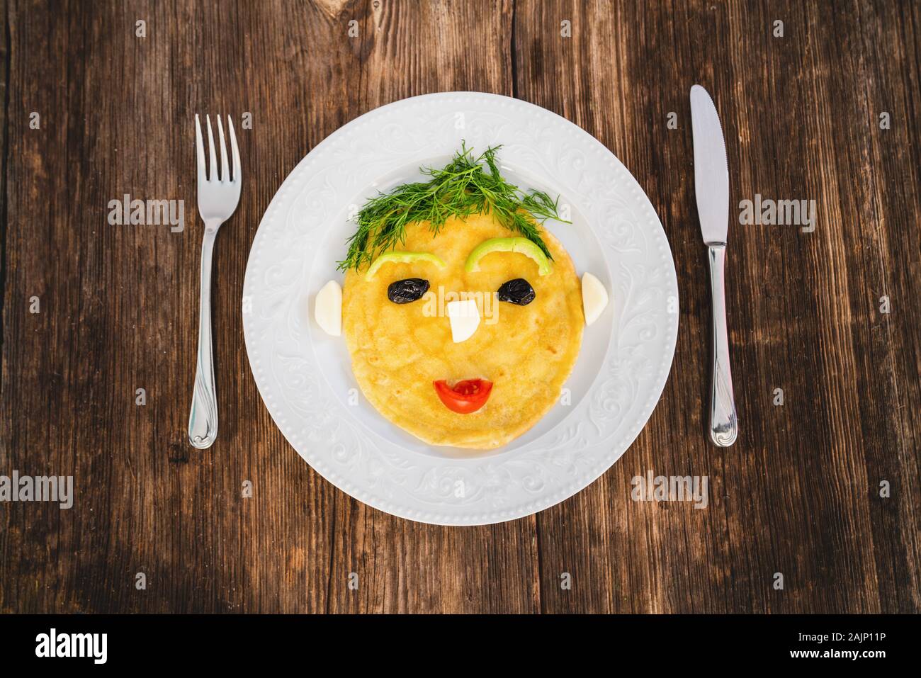 Divertenti omelette preparate con volto umano forma per bambini su uno sfondo di legno. Foto Stock
