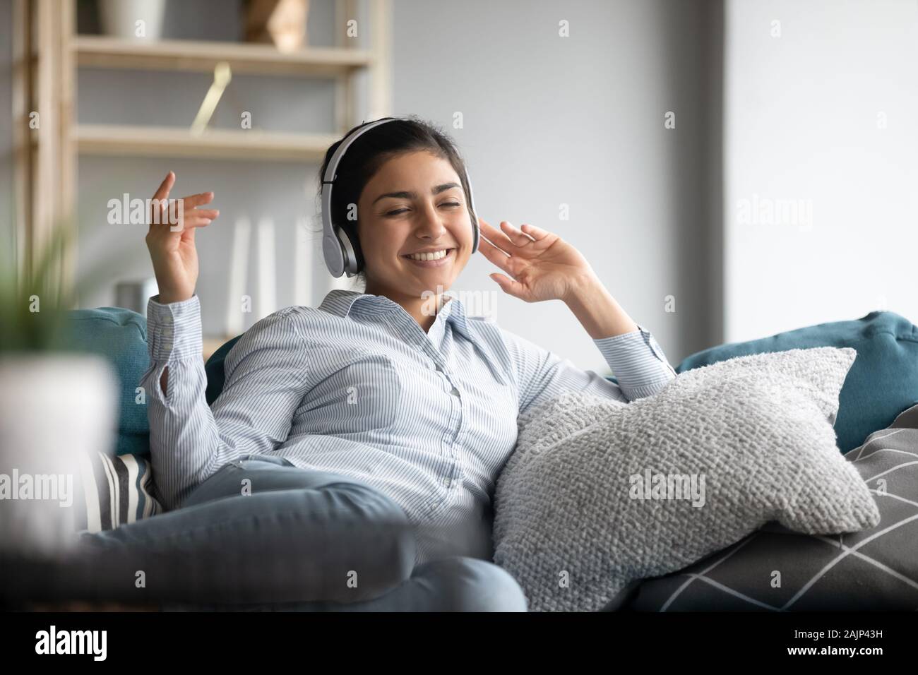 Sorridente ragazza indiana indossare le cuffie relax sul divano ascoltando musica Foto Stock