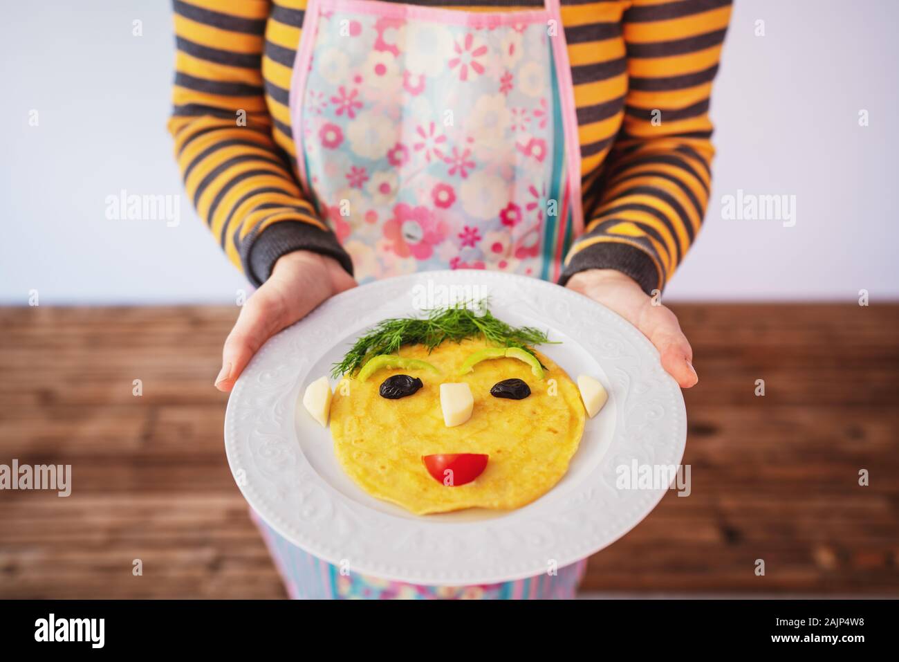 Divertenti omelette preparate con volto umano forma servita da una donna. Foto Stock