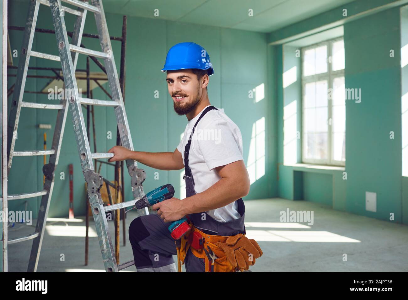 Builder contraente uomo barbuto in casco sorridere mentre si trova in corrispondenza di un sito in costruzione. Foto Stock