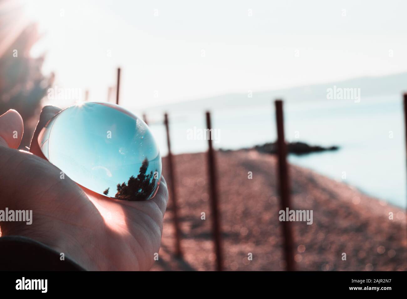 Mano che tiene un bicchiere di cristallo emisfero, riflessi blu del cielo circostante e del mare. Foto Stock
