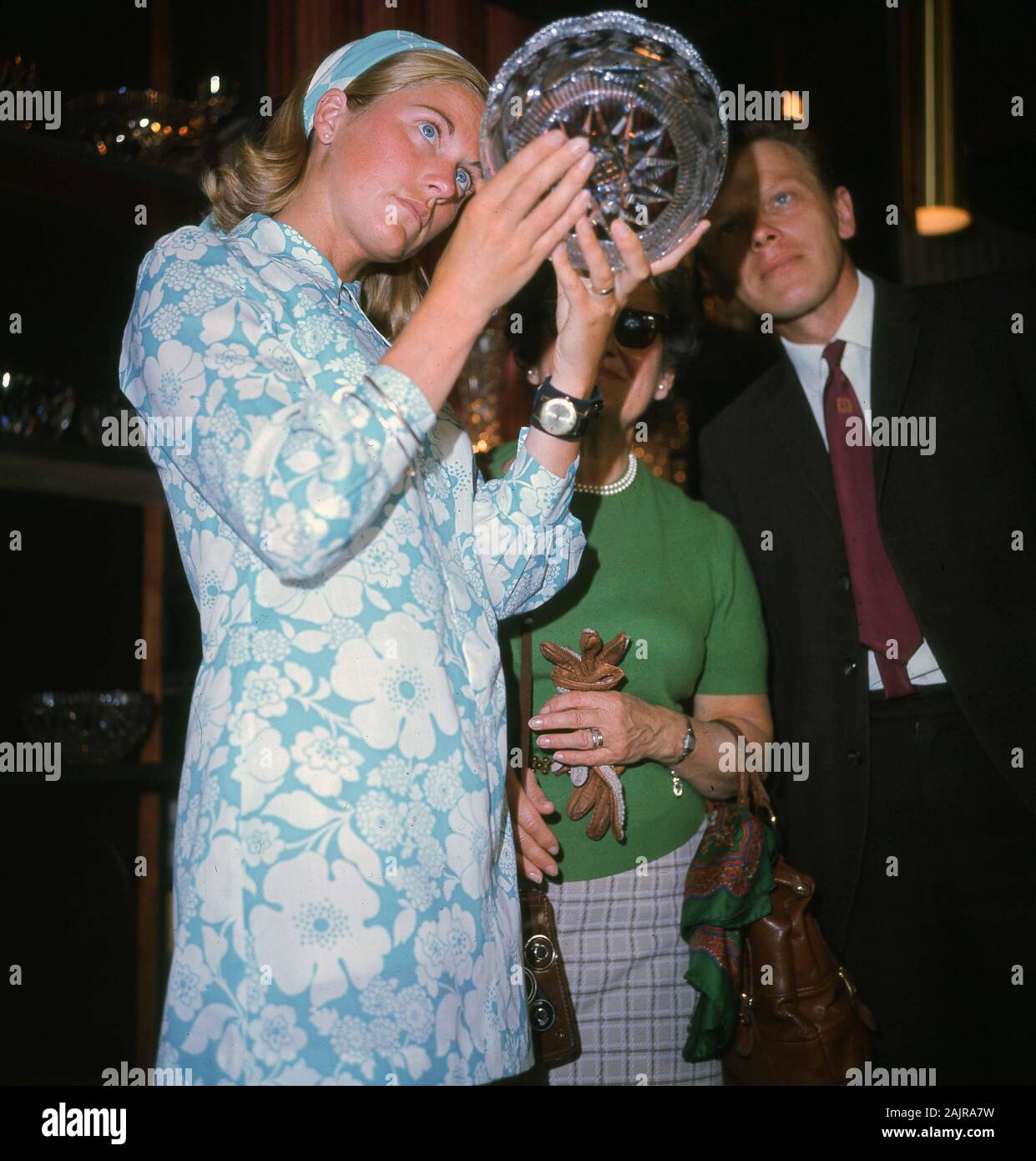 1960s, storico, una giovane signora in un abito a motivi floreali blu chiaro dell'epoca che studia una ciotola di vetro tagliata di recente produzione, Inghilterra, Regno Unito. Foto Stock