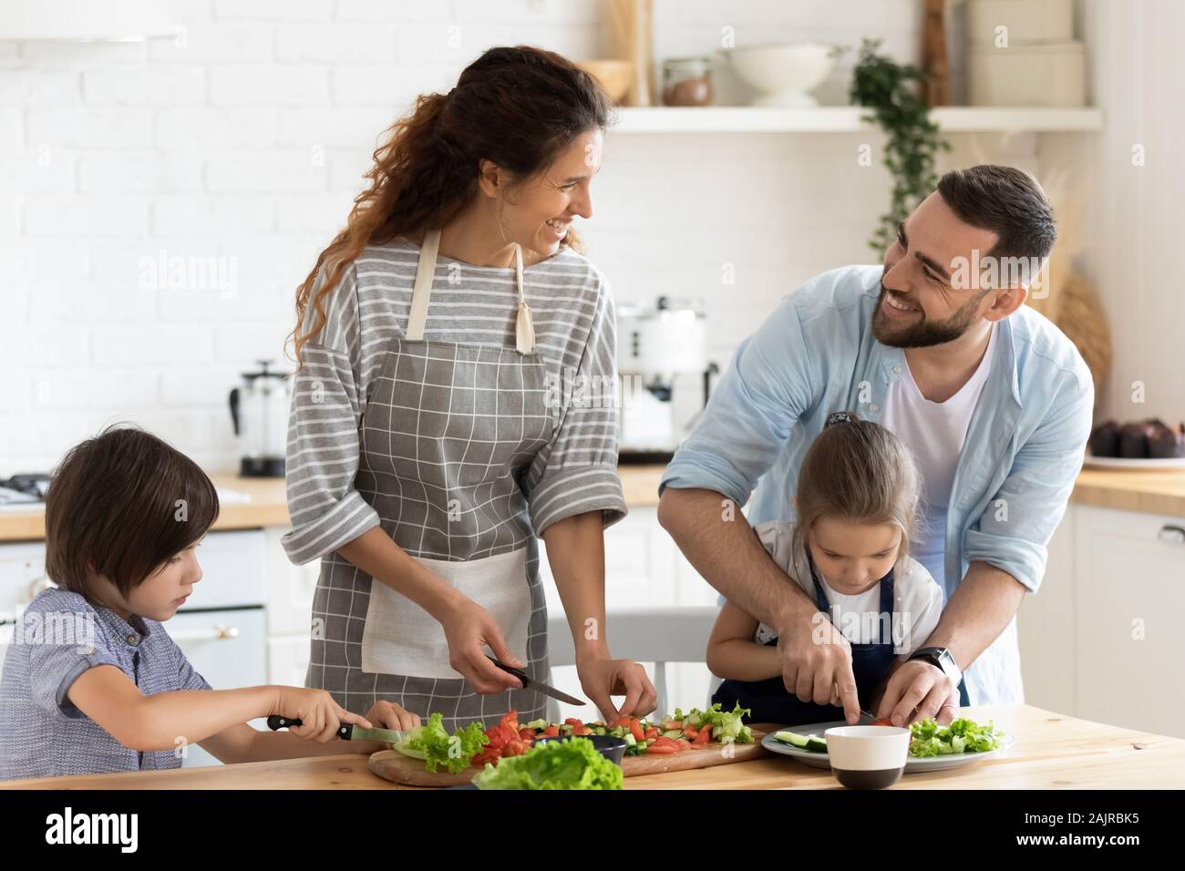 La famiglia completa con i bambini in chat e la preparazione di sana insalata vegetariana Foto Stock