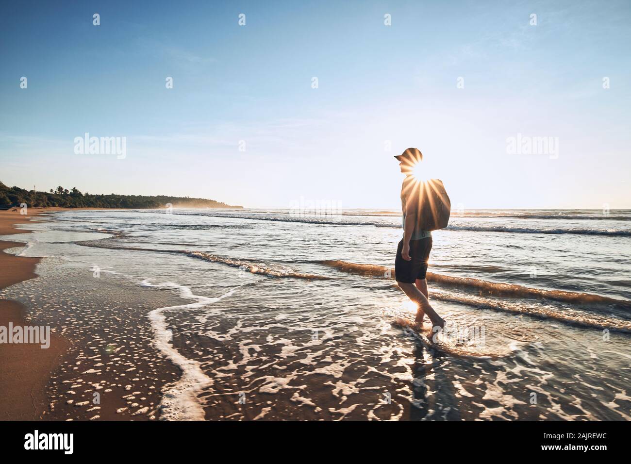 Giovane uomo con zaino camminare sulla sabbia tropicale sulla spiaggia. Costa di Sri Lanka a bellissima alba. Foto Stock