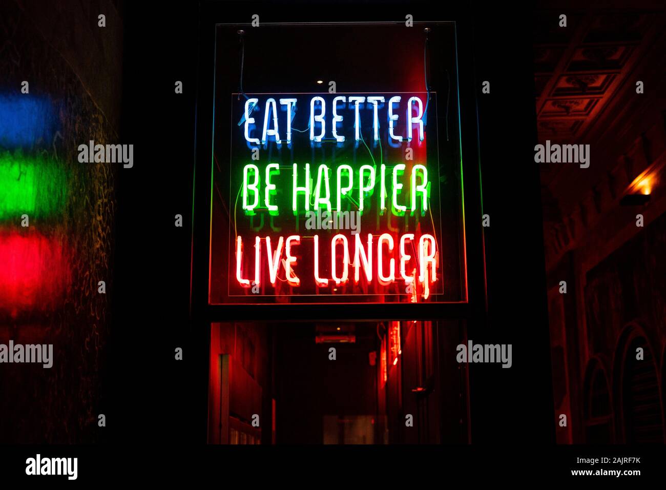 Led colorati e luci al neon sign dove mette: "Mangiare meglio, essere felici e vivere più a lungo". Concetto di salute e cibo. Foto Stock