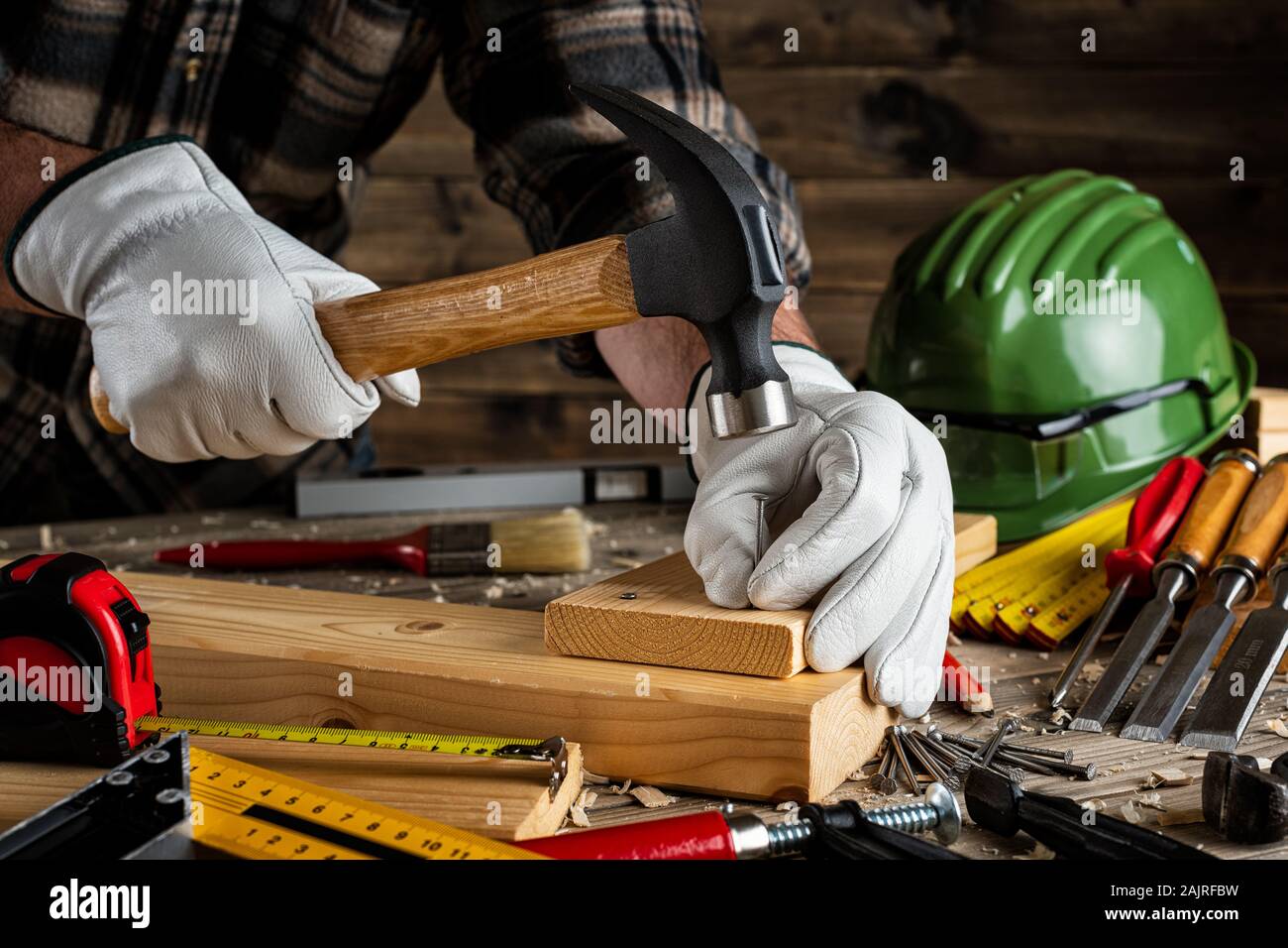 Close-up. Carpenter con le mani protette da guanti, con martello e chiodi fissa una tavola di legno. Industria edile, fai da te. Lavori in legno Foto Stock