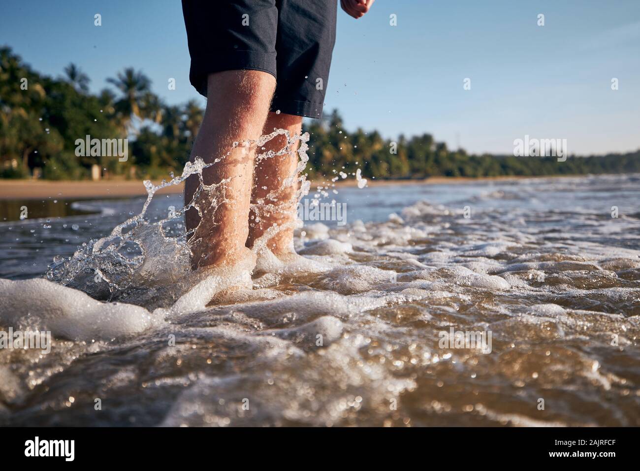 Le gambe del giovane uomo in mare contro tropicale sulla spiaggia di sabbia. Foto Stock