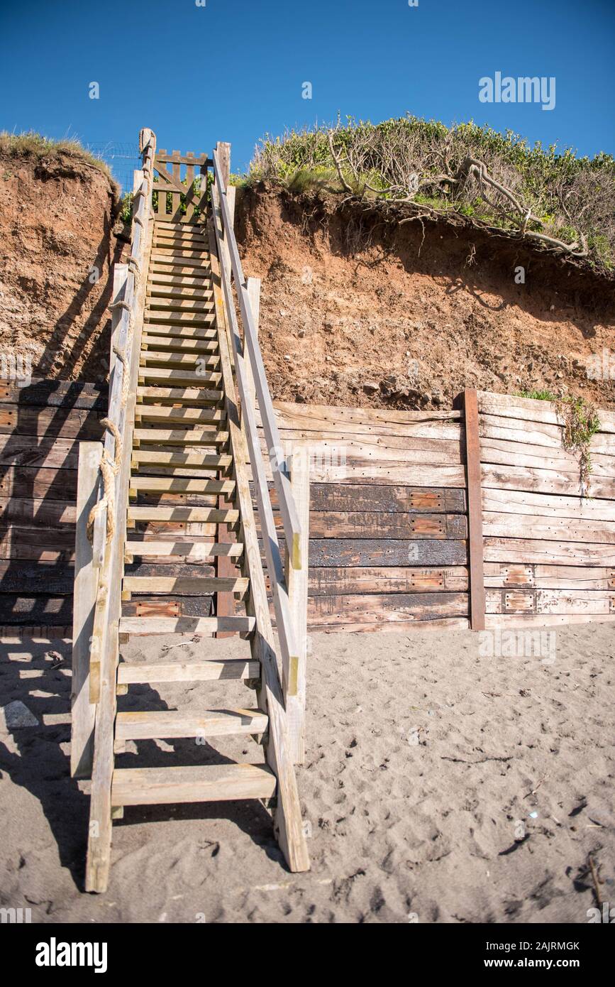 Scala in legno da spiaggia a spiaggia sabbiosa a downderry, cornovaglia che mostra erosione costiera su entrambi i lati e legno difese costiere Foto Stock