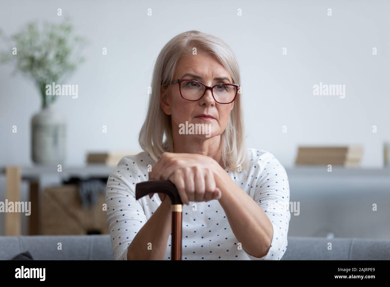 Triste senior donna tenere bastone da passeggio sentirsi soli a casa Foto Stock