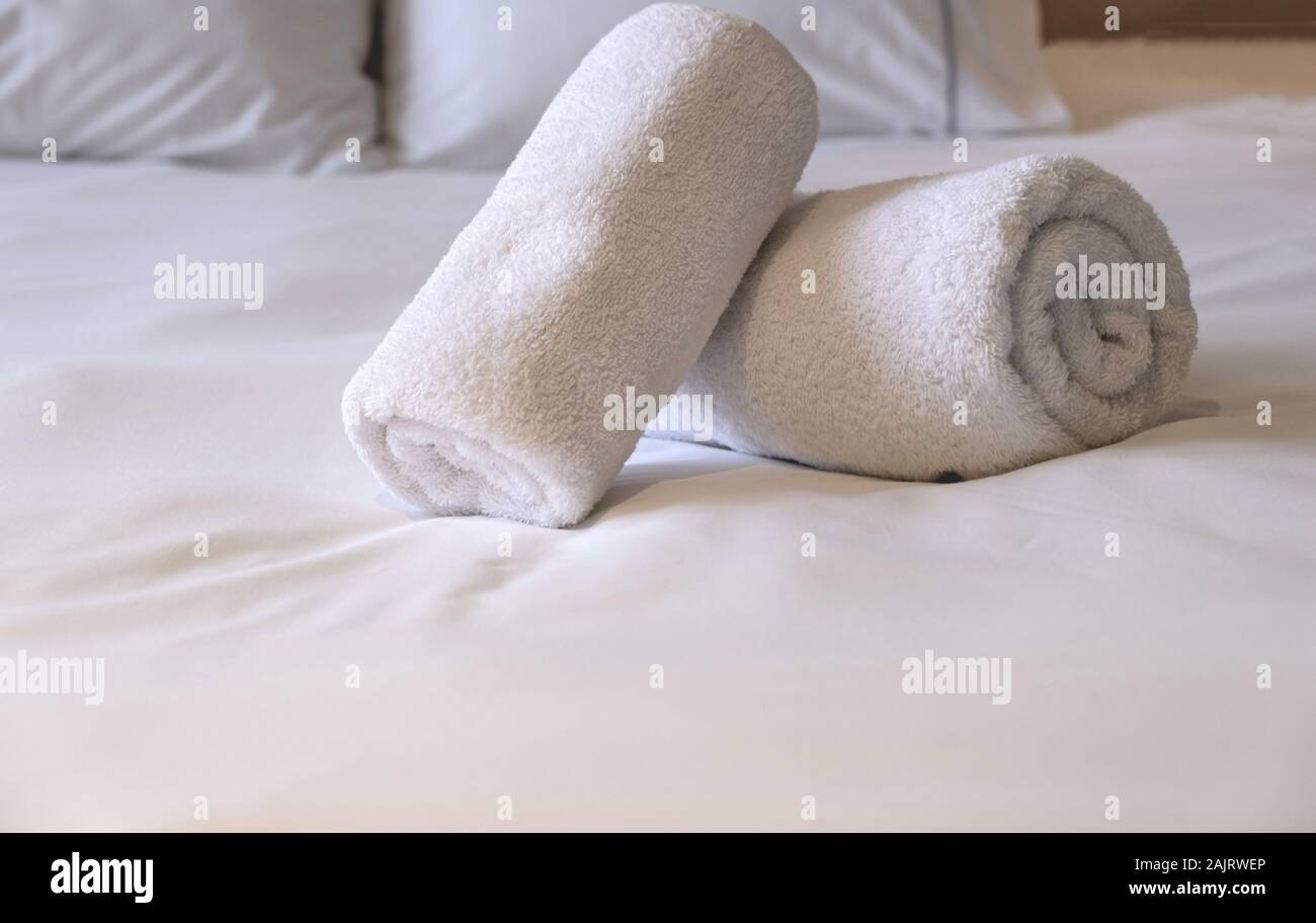 Hotel asciugamani. Bianchi e soffici, laminato asciugamani da bagno, le lenzuola e i cuscini sul letto, camera da letto dettaglio interni. Vista ravvicinata. Foto Stock