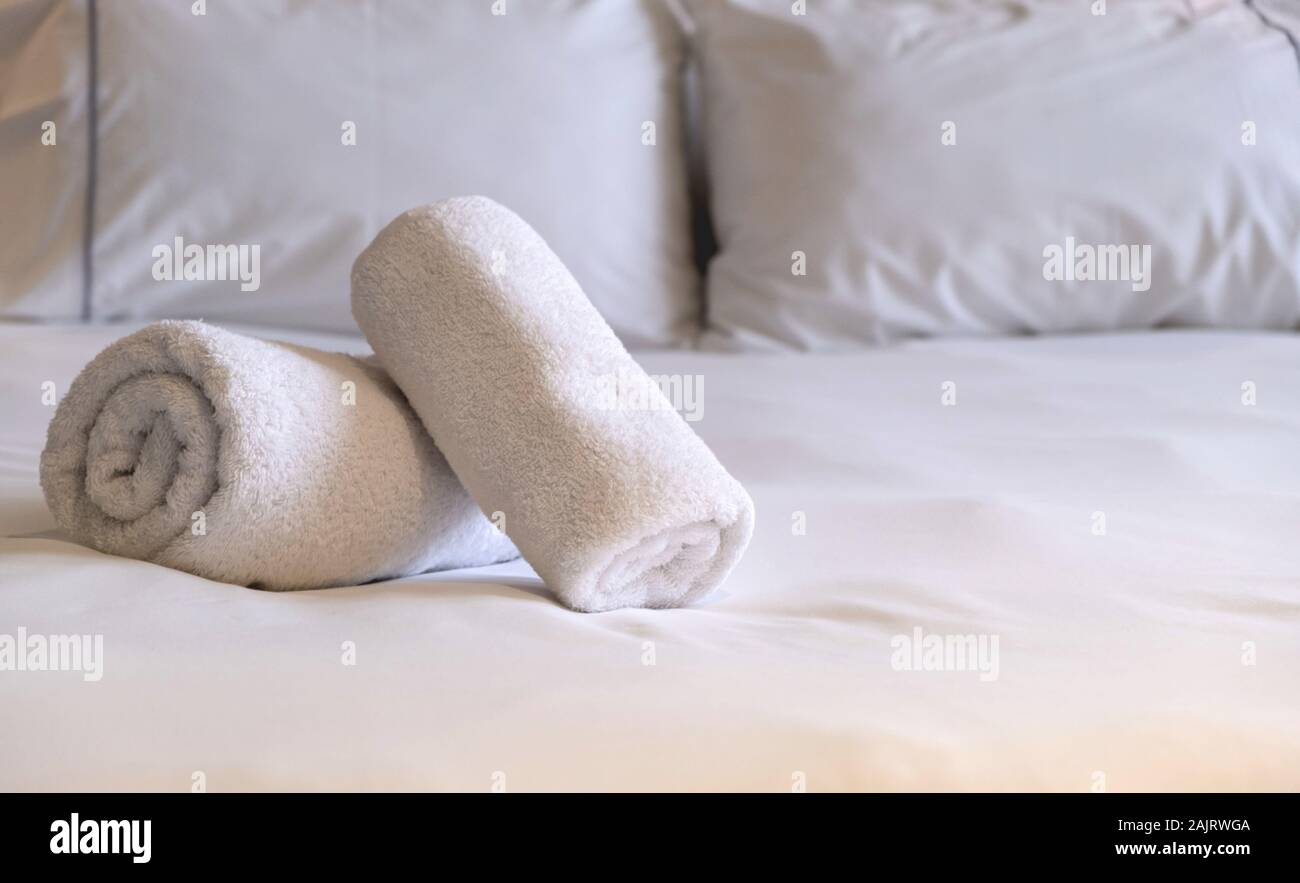 Hotel asciugamani. Bianchi e soffici, laminato asciugamani da bagno, le lenzuola e i cuscini sul letto, camera da letto dettaglio interni. Vista ravvicinata. Foto Stock