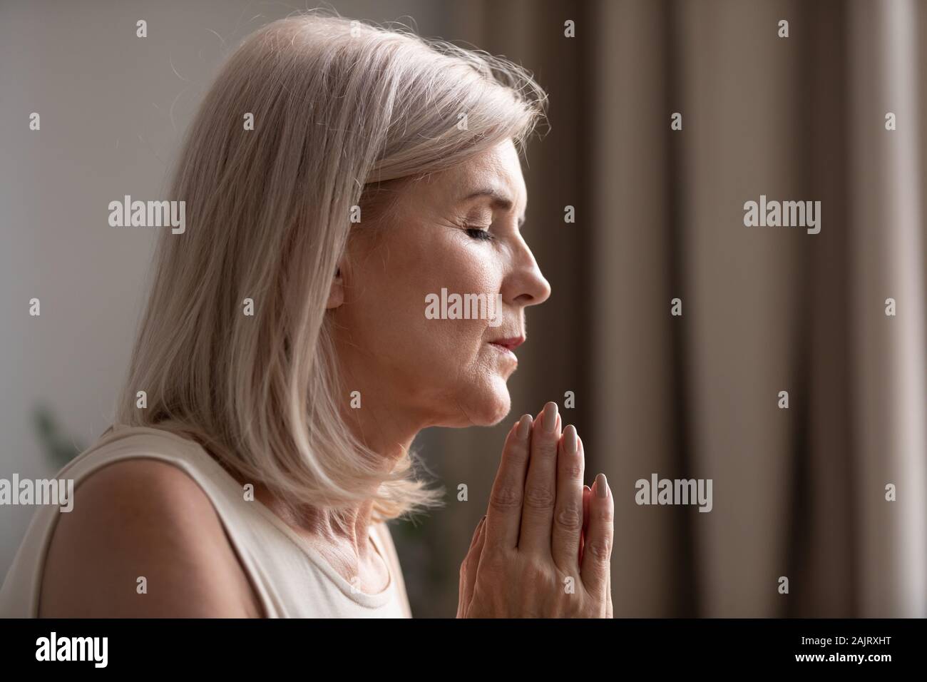 Close up di senior donna credente pregando in casa Foto Stock