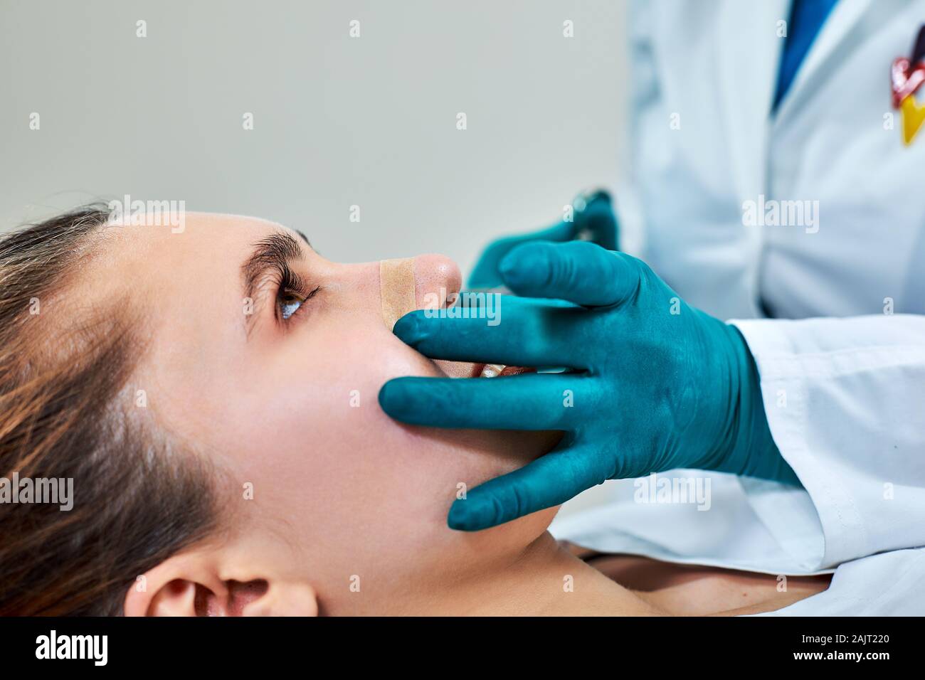 Lady con gesso sul naso, medico esaminare pazienti viso dopo un intervento di chirurgia plastica. Foto Stock