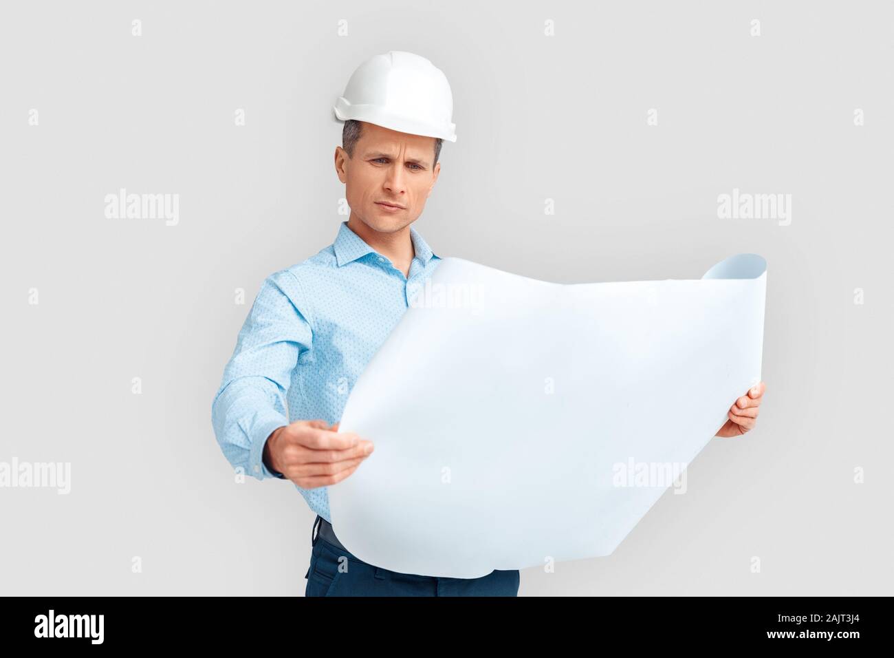 Costruzione. Uomo maturo in hardhat in piedi isolato su bianco con blueprint lo studio in questione Foto Stock