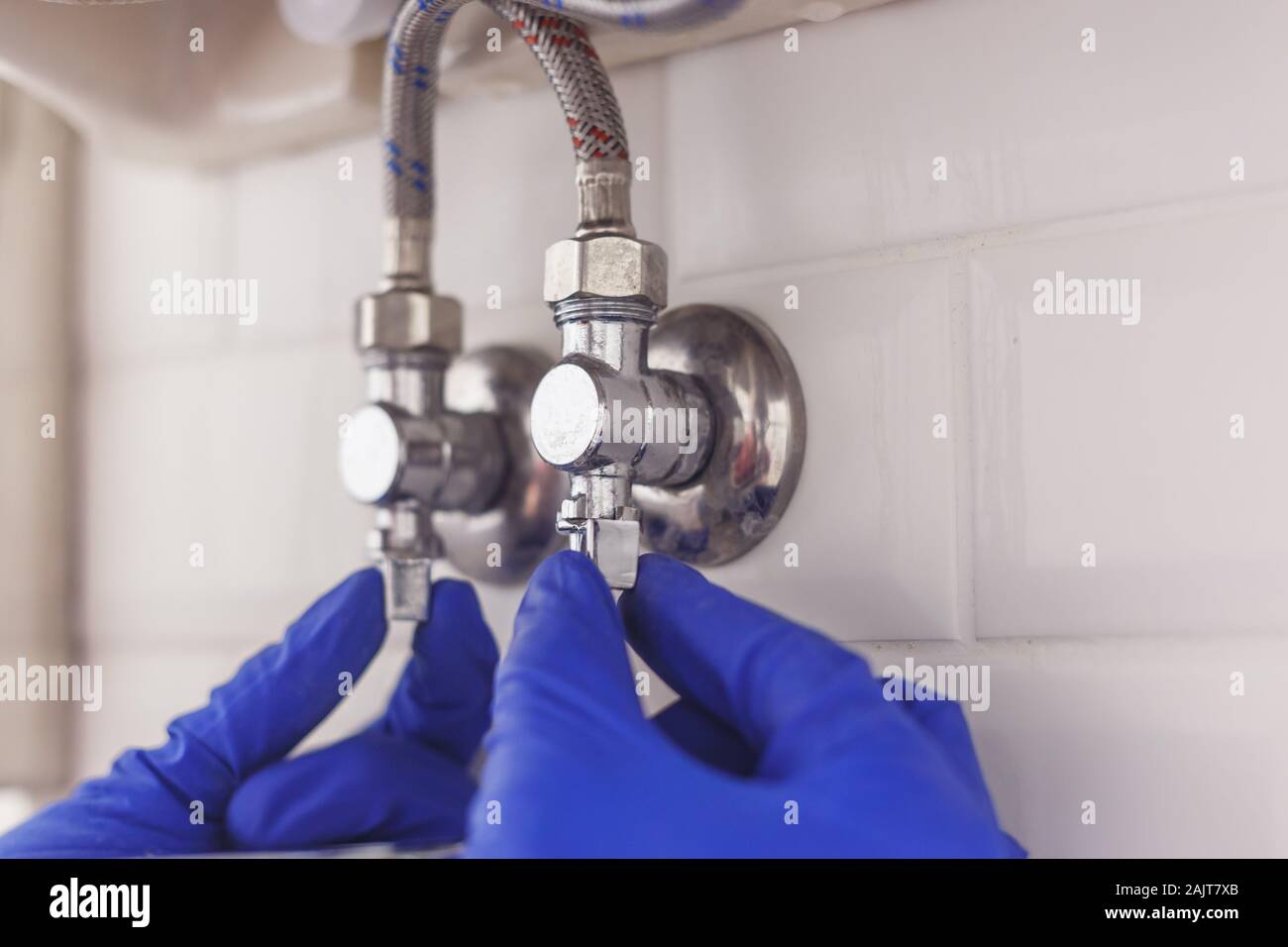 Plumber angolo di chiusura delle valvole di adduzione acqua calda e fredda sotto il lavandino per tubi flessibili di manutenzione o sostituire il rubinetto. Foto Stock
