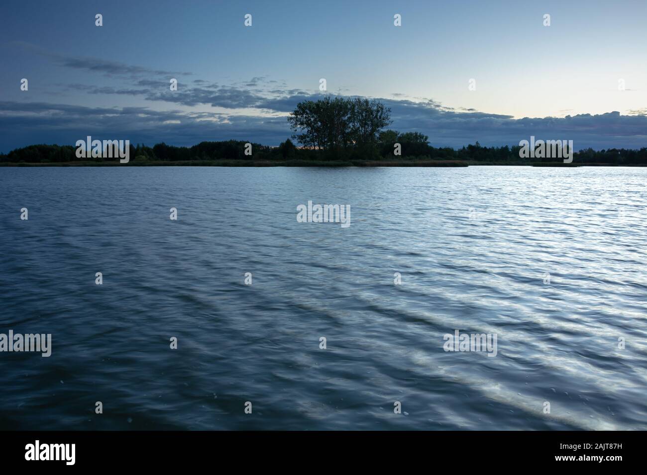 Alberi sulla riva di un lago calmo e nuvole di sera Foto Stock