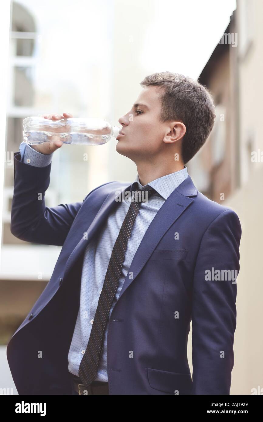 Uomo d affari con suit tenendo la bottiglia di acqua potabile e all'aperto. Il giovane uomo d affari bere acqua fresca Foto Stock
