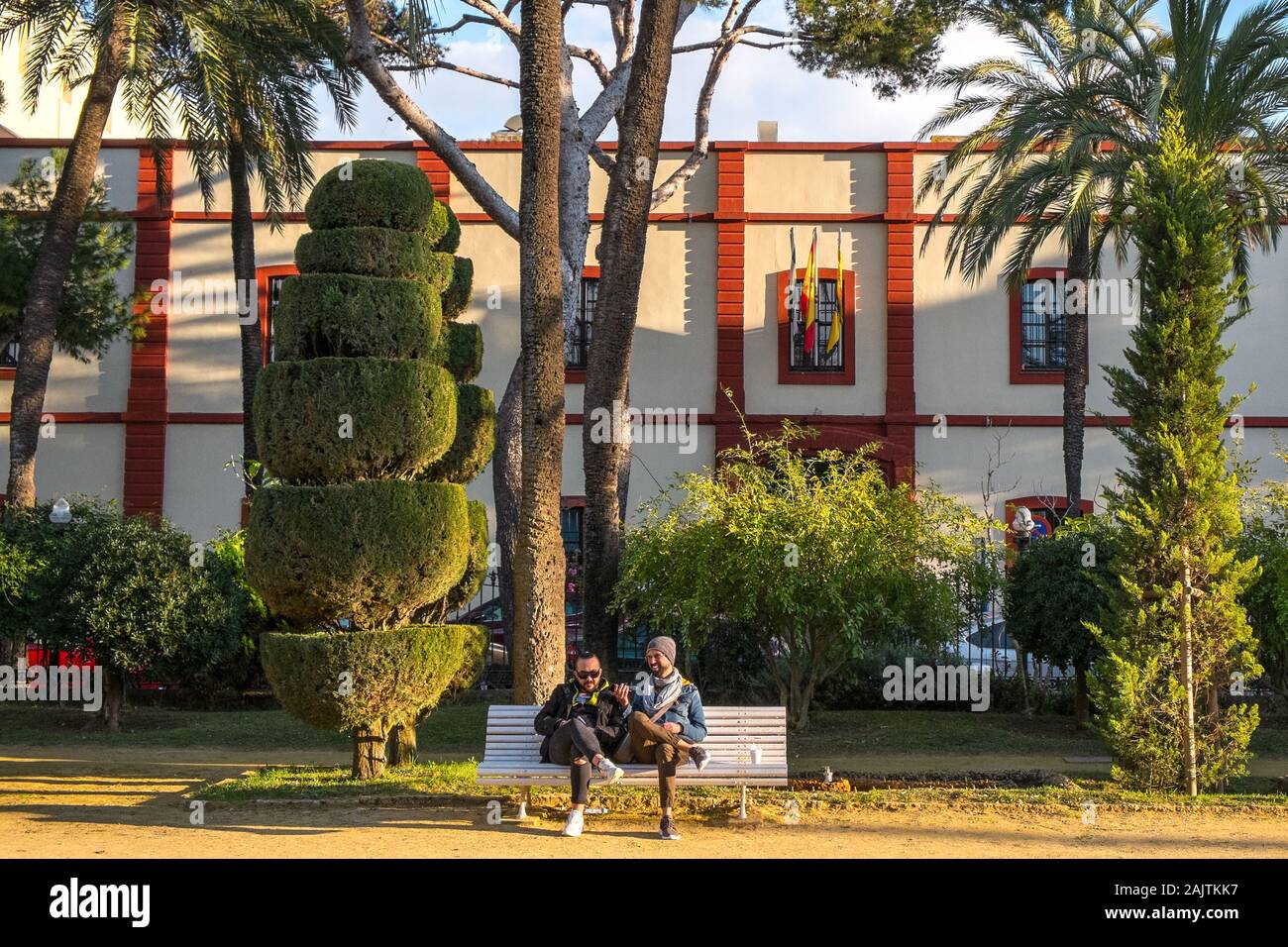 Due uomini siedono su una panchina del parco in un giardino paesaggistico, Cádiz, Spagna Foto Stock