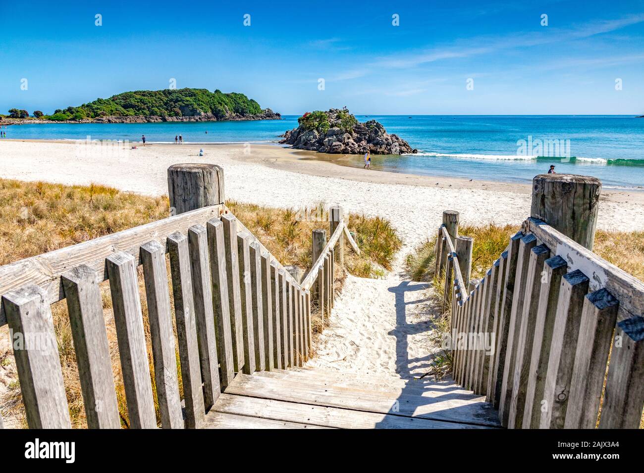 9 Dicembre 2018: Mount Maunganui, Baia di Planty, Nuova Zelanda - scalini per scendere in spiaggia su una bella giornata d'estate, con una piccola isola e la gente a piedi.. Foto Stock