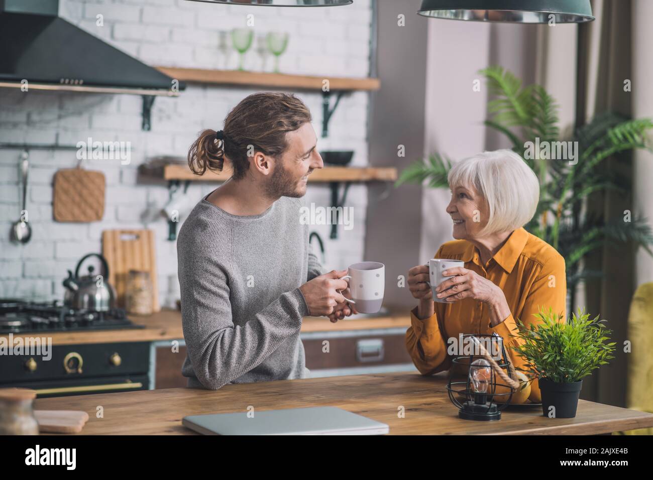 Grey-haired mom e suo figlio seduto in cucina Foto Stock