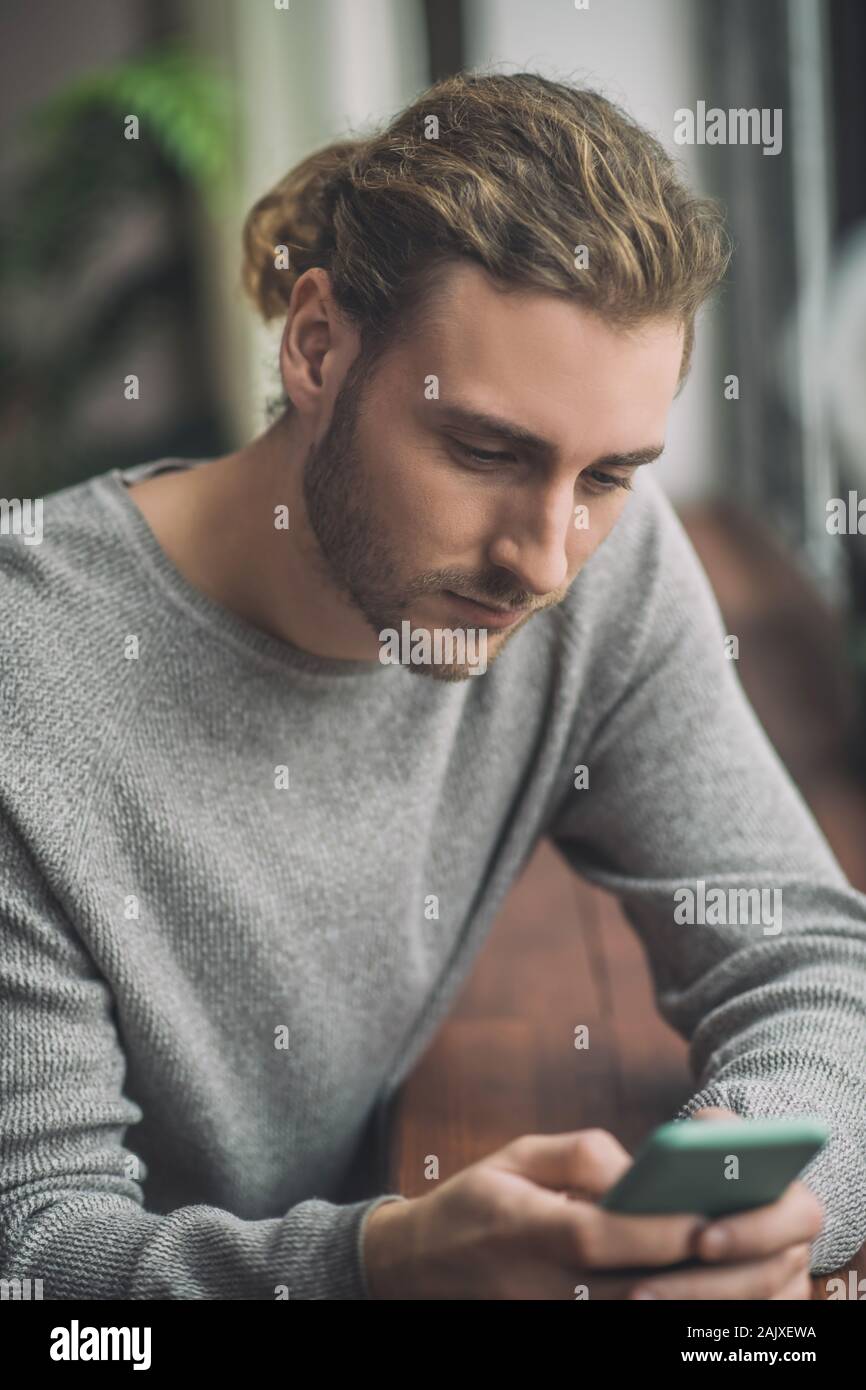 Giovani barbuto uomo bello in grigio osservando il suo telefono Foto Stock