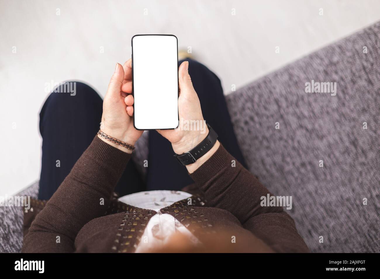 Vista superiore del senior lady in piedi sul divano con uno smartphone nelle mani. Persona in possesso di nero smartphone isolato schermo bianco e vuoto vuoto. White scre Foto Stock