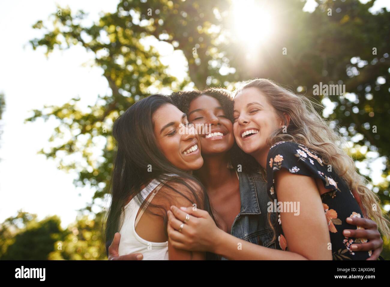 Ritratto di un felice gruppo multietnico amiche abbracciando e abbracciare ogni altra ridere e divertimento all'aperto in un parco Foto Stock