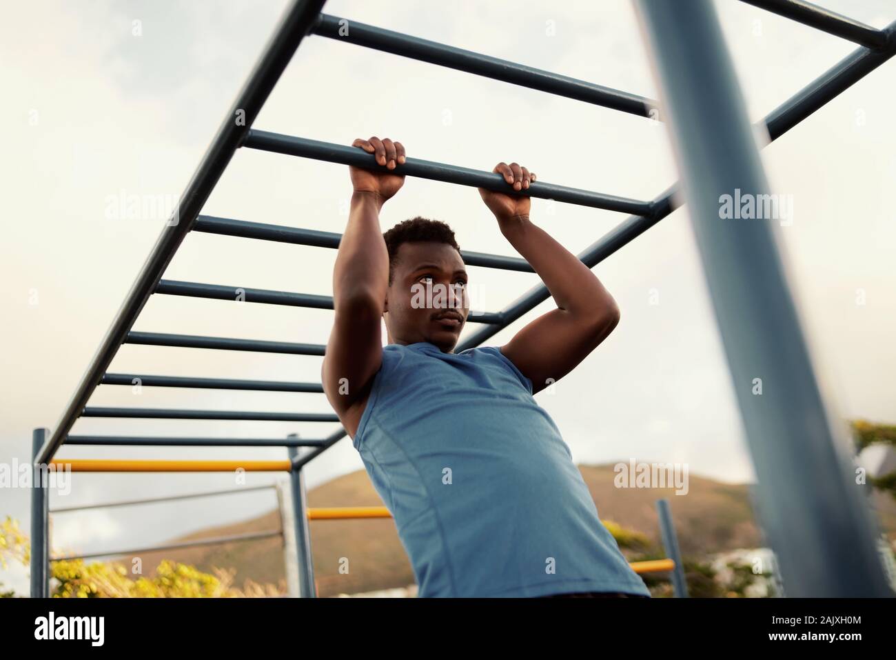 African American giovane esercitando sulle barre di scimmia per la parte superiore del corpo in un moderno parco calisthenics all'aperto in una giornata di sole Foto Stock