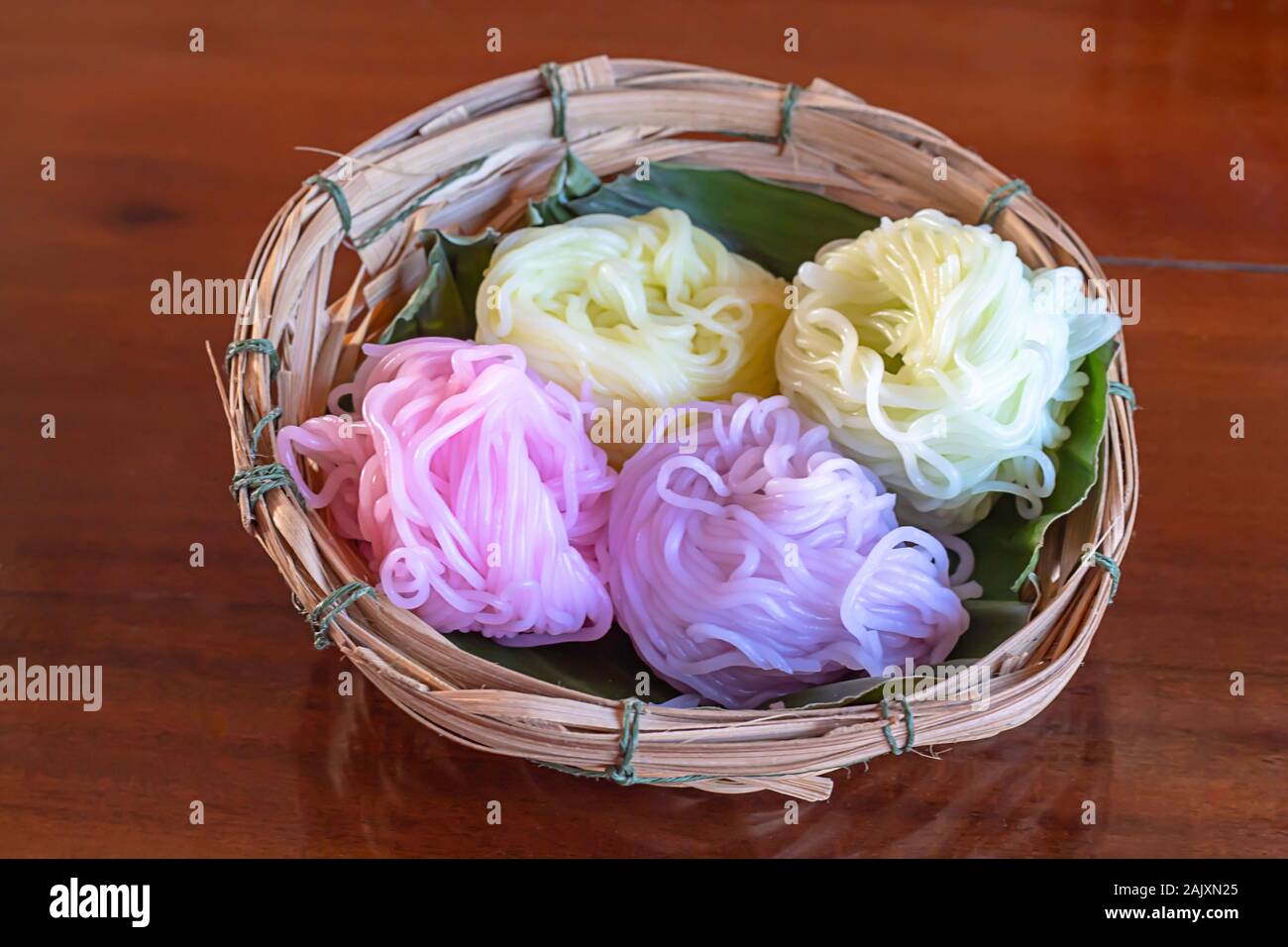 Colorato spaghetti di riso su una foglia di banano in un cestello di bambù sul tavolo. Foto Stock