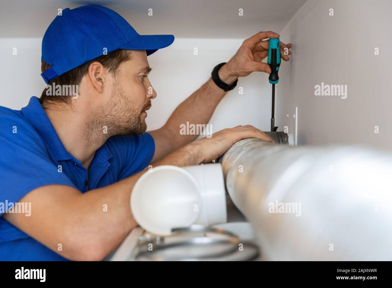 Tecnico di impianti di termoventilazione riparazione flessibile tubo in alluminio per alloggiare il sistema di ventilazione Foto Stock
