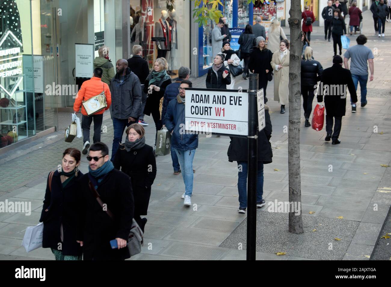 Giovane shopping a Natale a piedi passato Adamo ed Eva Corte W1 strada segno su Oxford Street nel West End di Londra Inghilterra KATHY DEWITT Foto Stock