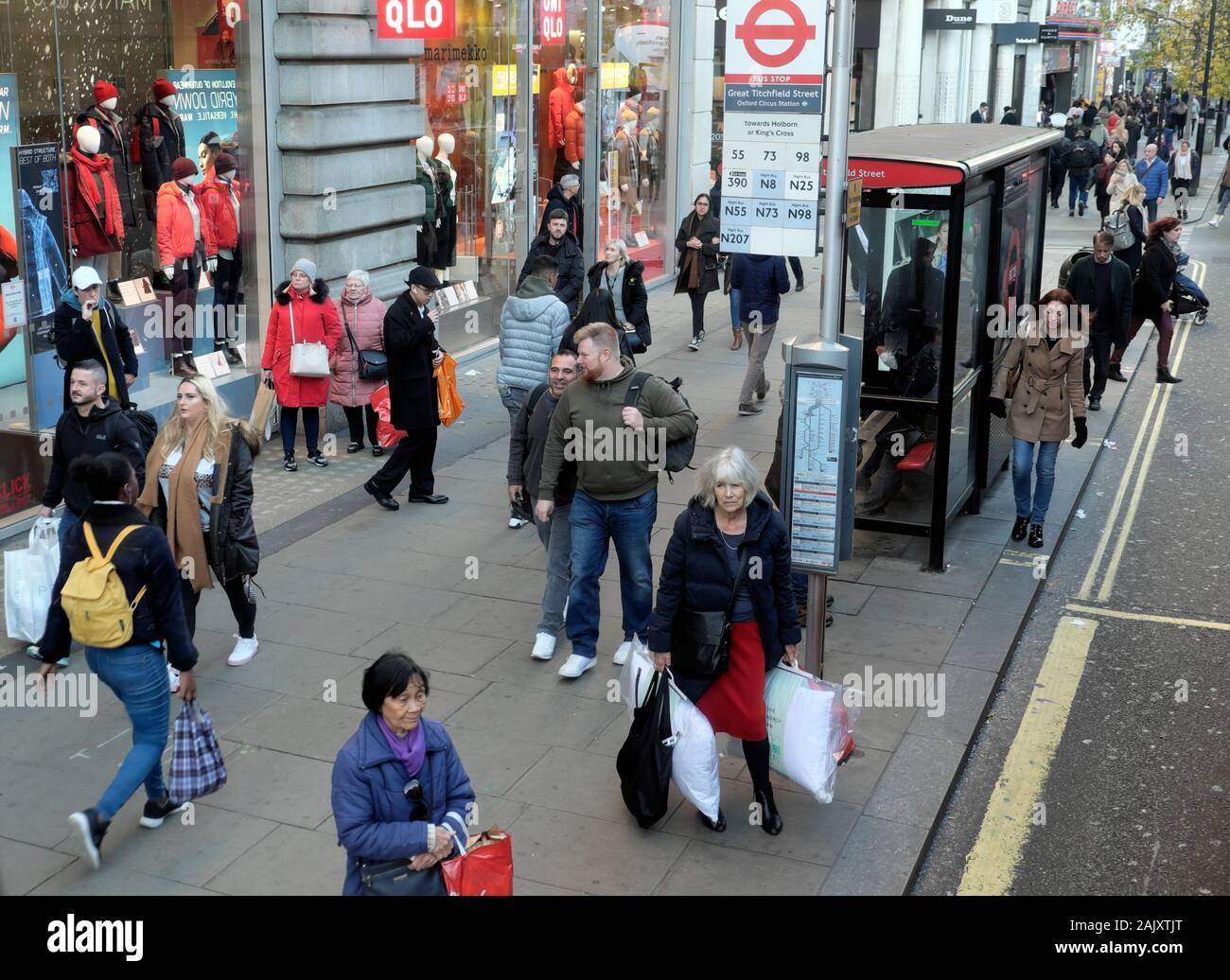 Gli acquirenti di persone che indossano abiti invernali in piedi in attesa di un autobus alla fermata fuori Uniqlo store in Oxford Street Londra Inghilterra KATHY DEWITT Foto Stock
