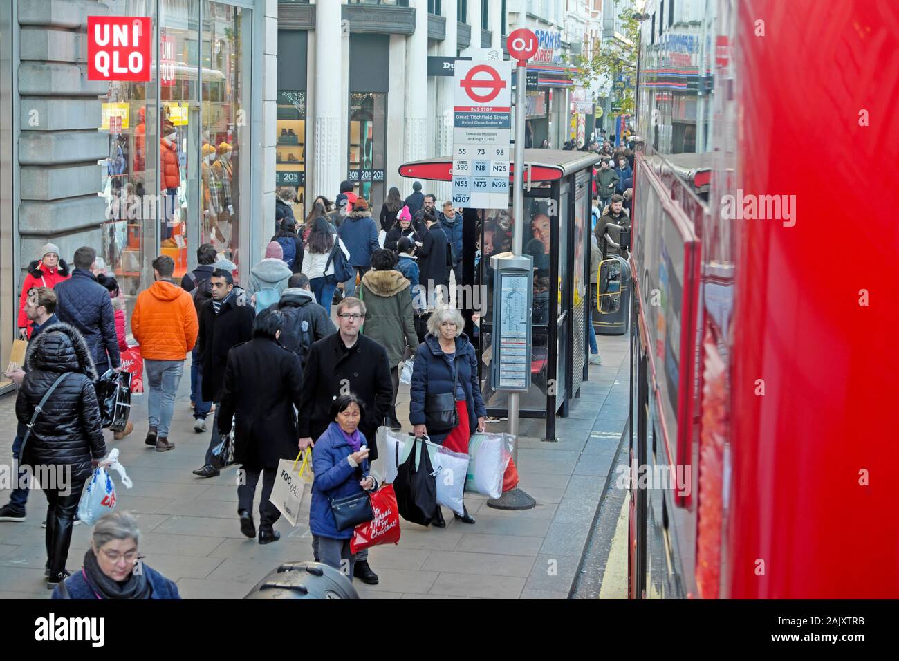 Gli acquirenti di persone che indossano abiti invernali in piedi in attesa di un autobus alla fermata fuori Uniqlo store in Oxford Street Londra Inghilterra KATHY DEWITT Foto Stock