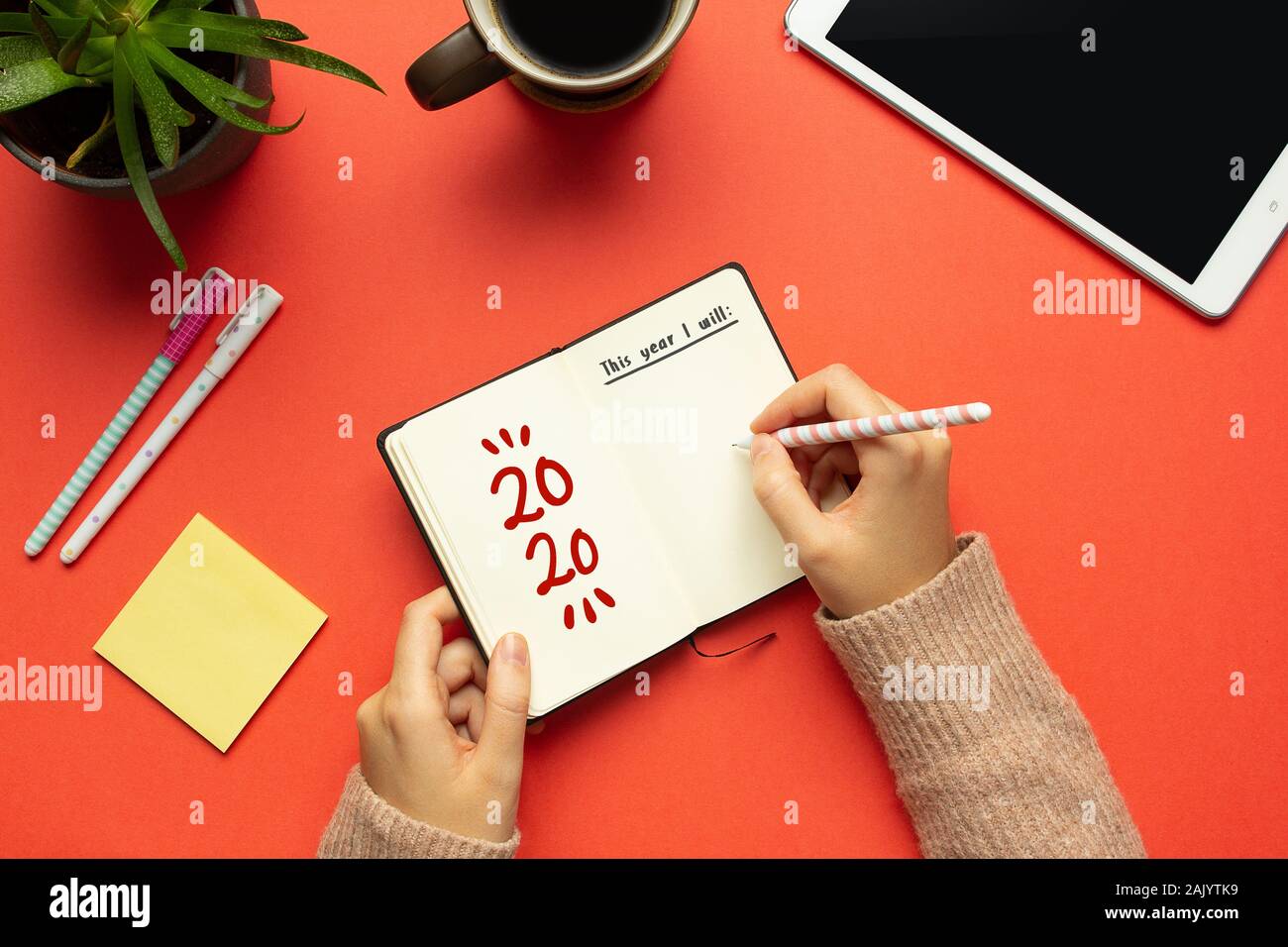 Stock Foto di una giovane donna le mani la scrittura in un 2020 anno nuovo notebook con lista di obiettivi e di oggetti su sfondo rosso Foto Stock