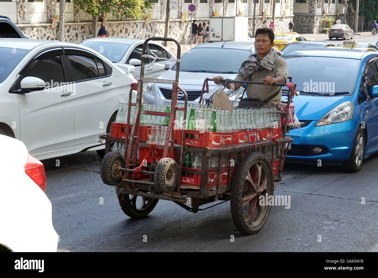 Uomo con vuoto soft drink bottiglie nel suo carrello motorizzato su strada trafficata. Foto Stock