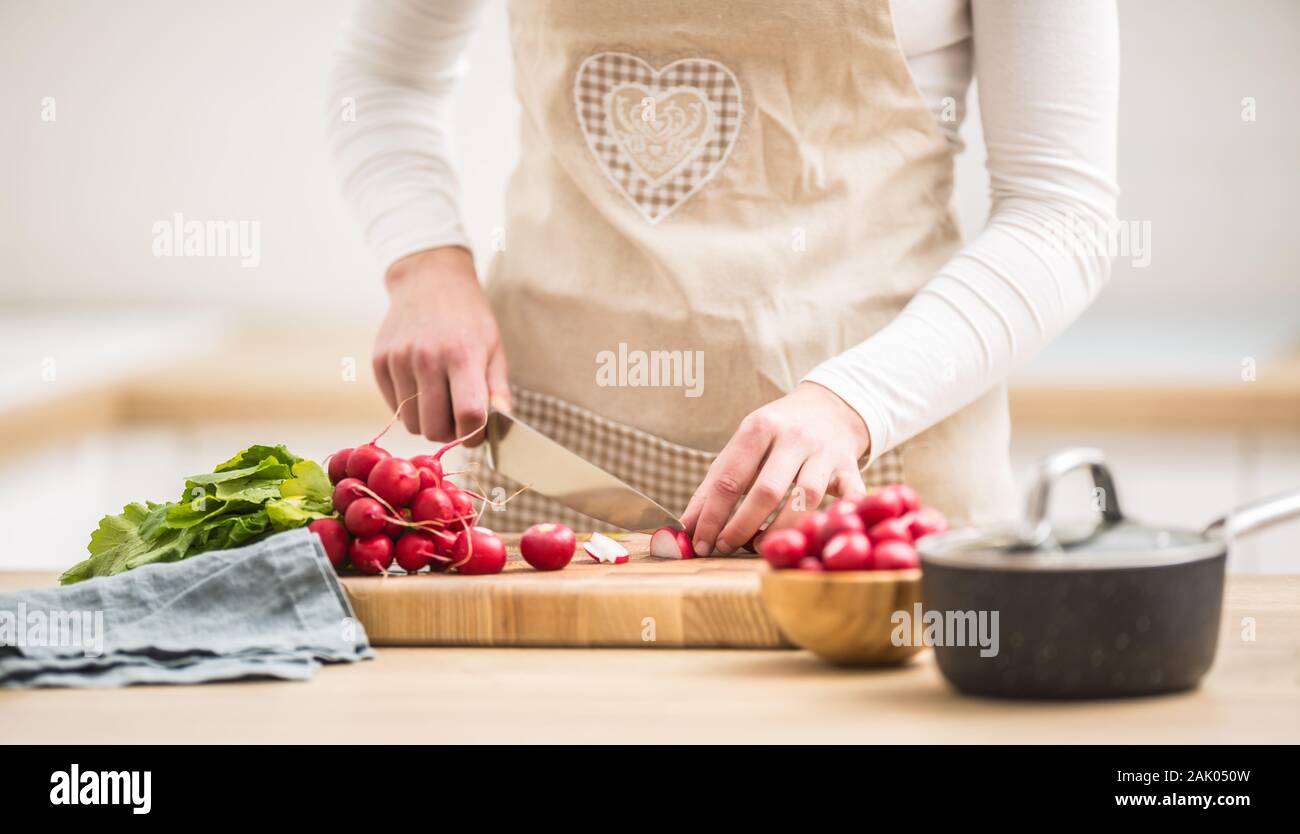 Donna affettamento rafano fresco a casa in cucina Foto Stock