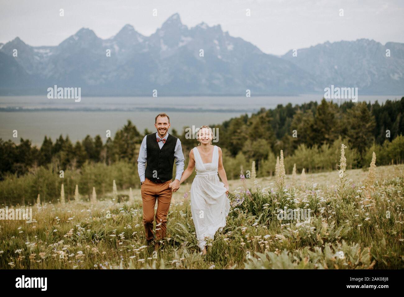 Felice sorridente sposi nuovi camminano attraverso il campo di fiori selvatici in Teton Foto Stock
