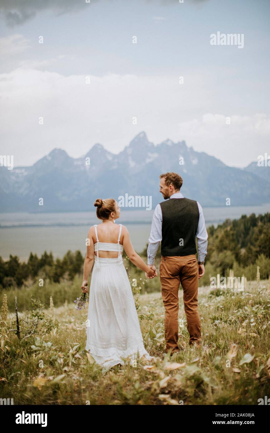 Gli sposi felici tengono le mani e guardano fuori i Teton in distanza Foto Stock