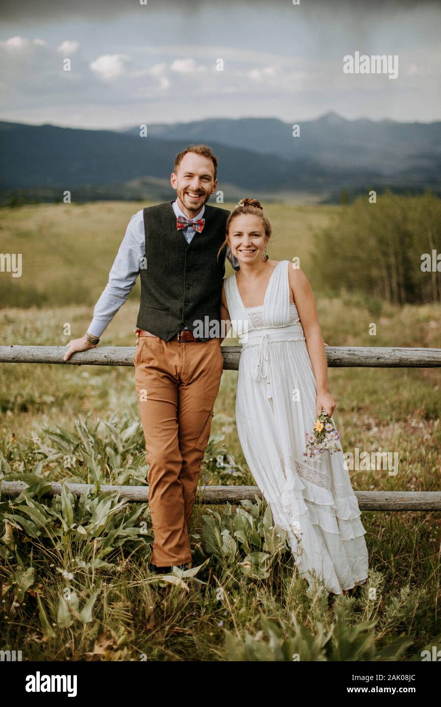 Sorridente sposa felice e sposo appoggiarsi contro recinzione in campo in Wyoming Foto Stock