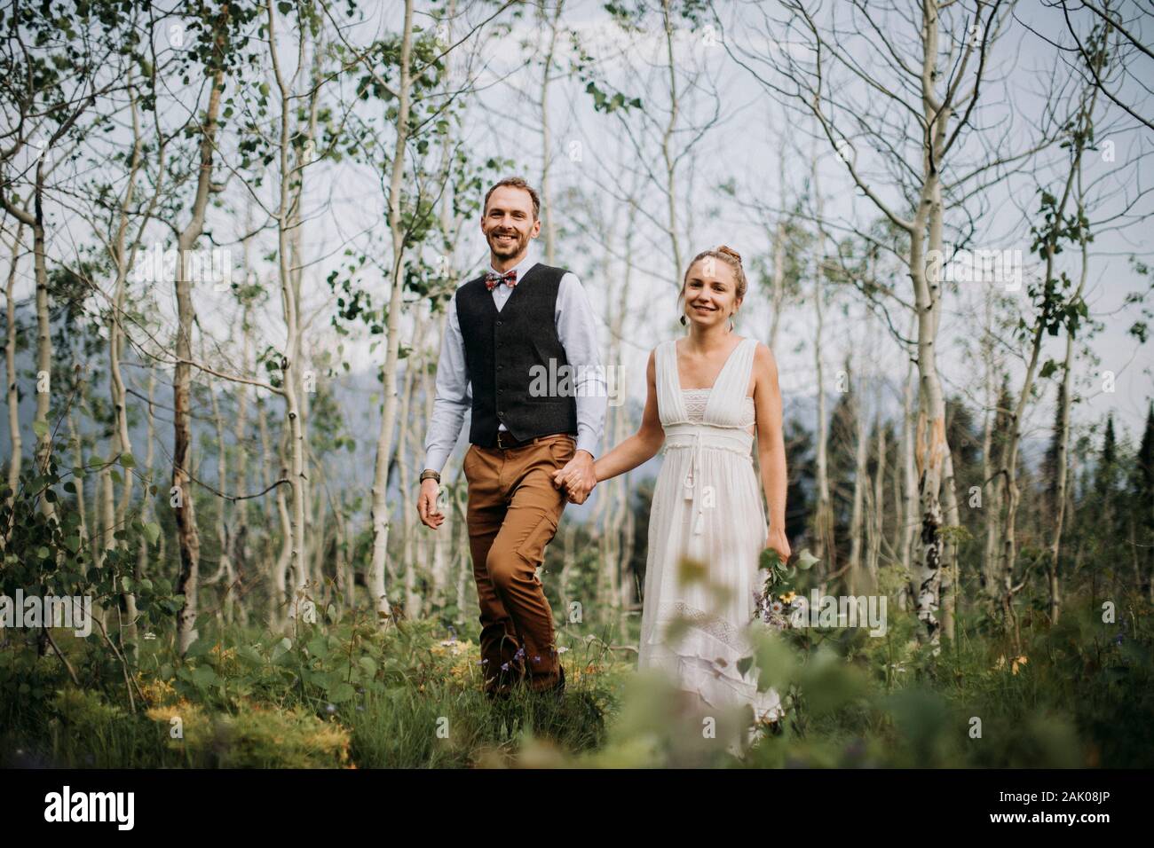 Gli sposi felici tengono le mani a piedi attraverso la foresta di betulla, Wyoming Foto Stock