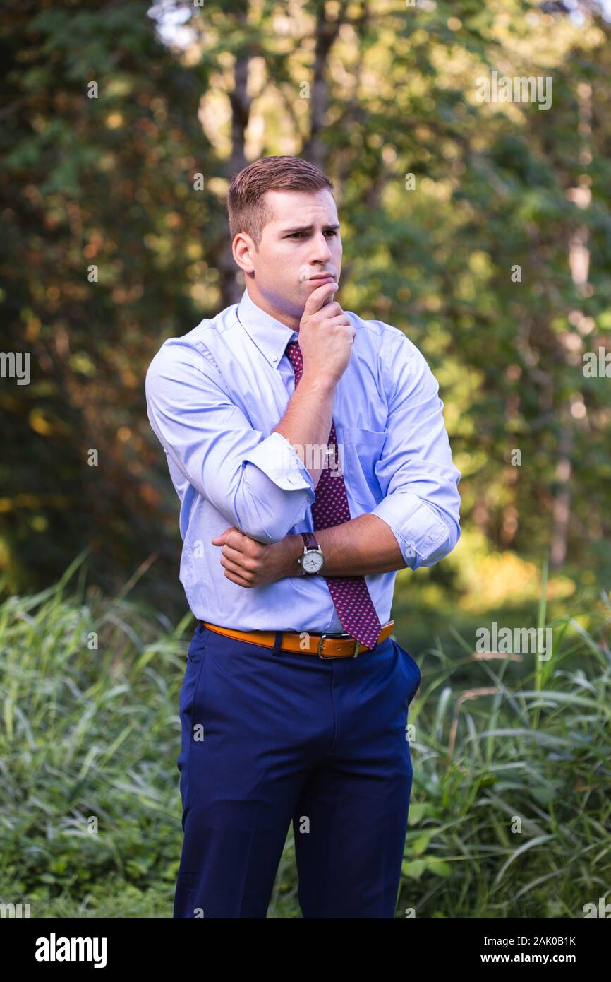 Giovane uomo fuori con mano sul mento profondo nel pensiero. Foto Stock