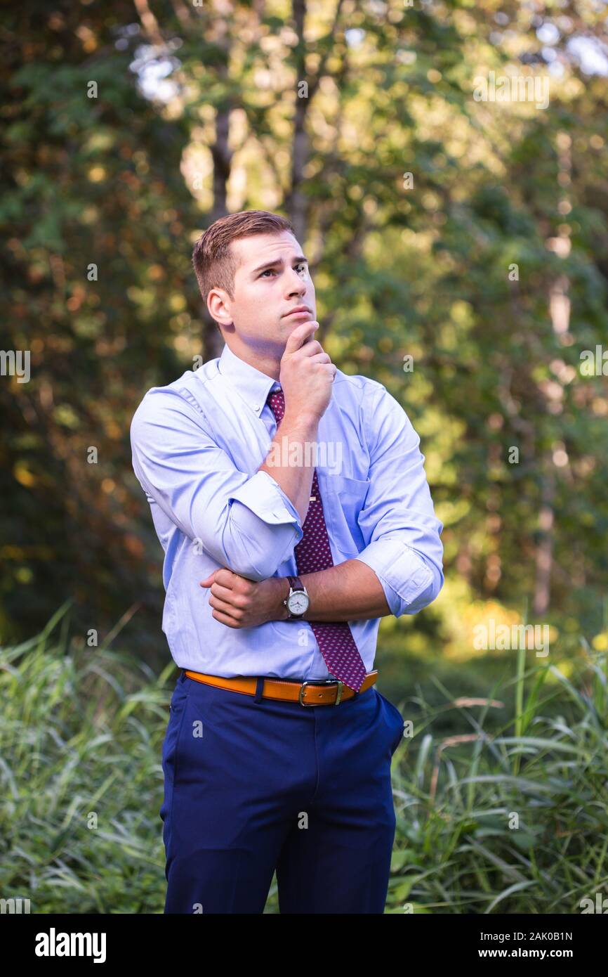 Giovane uomo in tuta si alza fuori, mano sul mento, profondo nel pensiero. Foto Stock