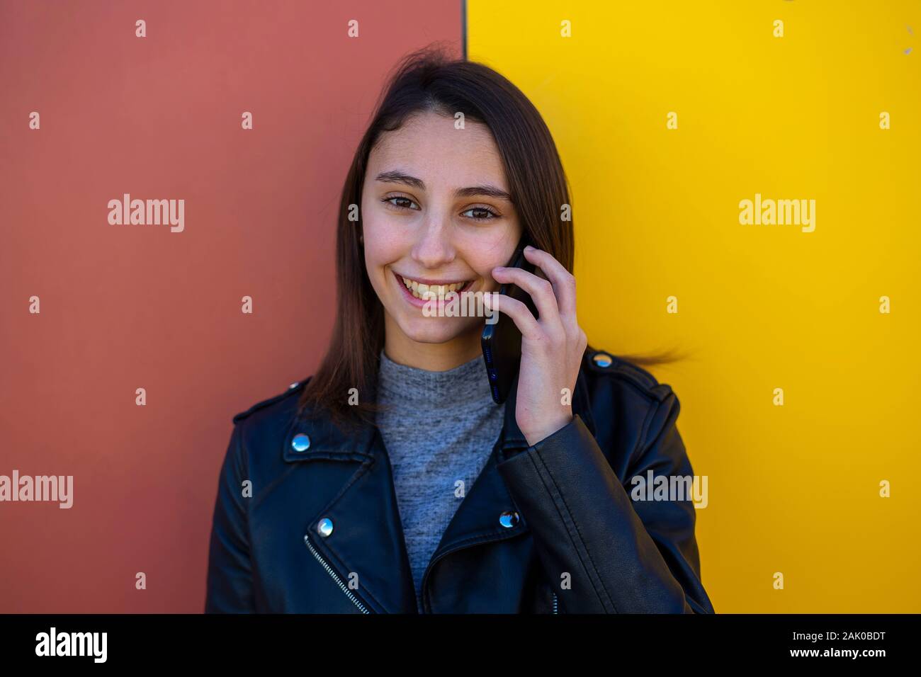 Giovane ed elegante Donna che parla al telefono su un giallo e marrone a sfondo mentre sorridente. Concetto di imprenditrice. Foto Stock