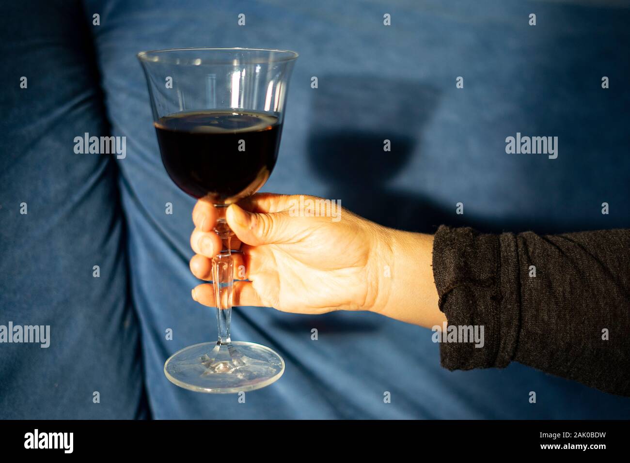 La mano di prendere un bicchiere di vino rosso sotto la luce del sole. Vino rosso in sfondo blu. Foto Stock