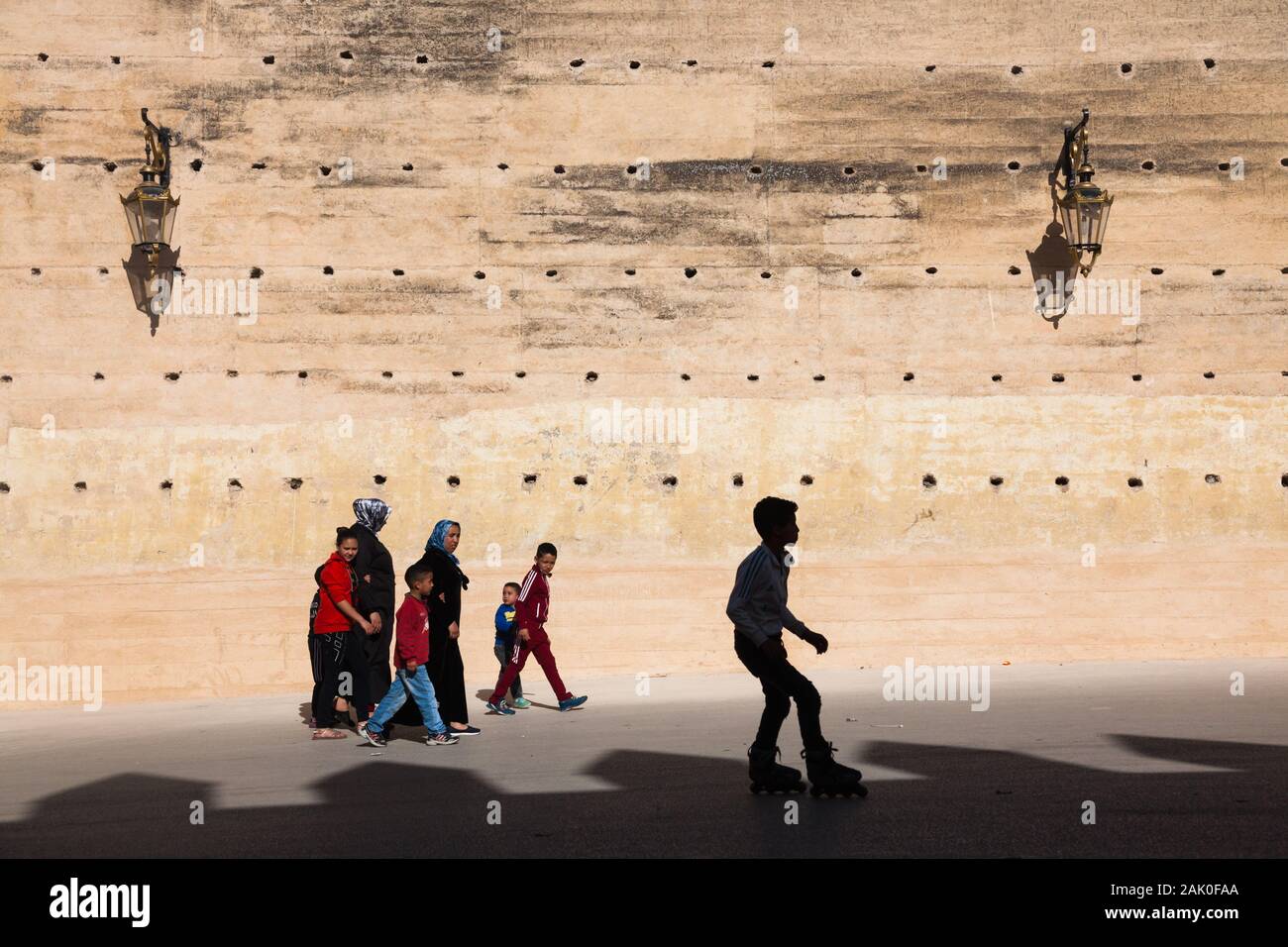 Tradizione e modernità - boy con i pattini e i pedoni (donne e bambini) nel pomeriggio scenario delle mura della città di Fès (fez), Marocco Foto Stock