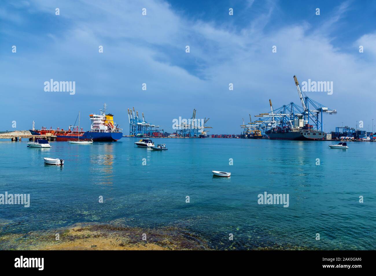 Una vista incredibile di un porto industriale con molte navi cargo vicino a gru edili sul mare sullo sfondo di un cielo blu a Malta. Foto Stock