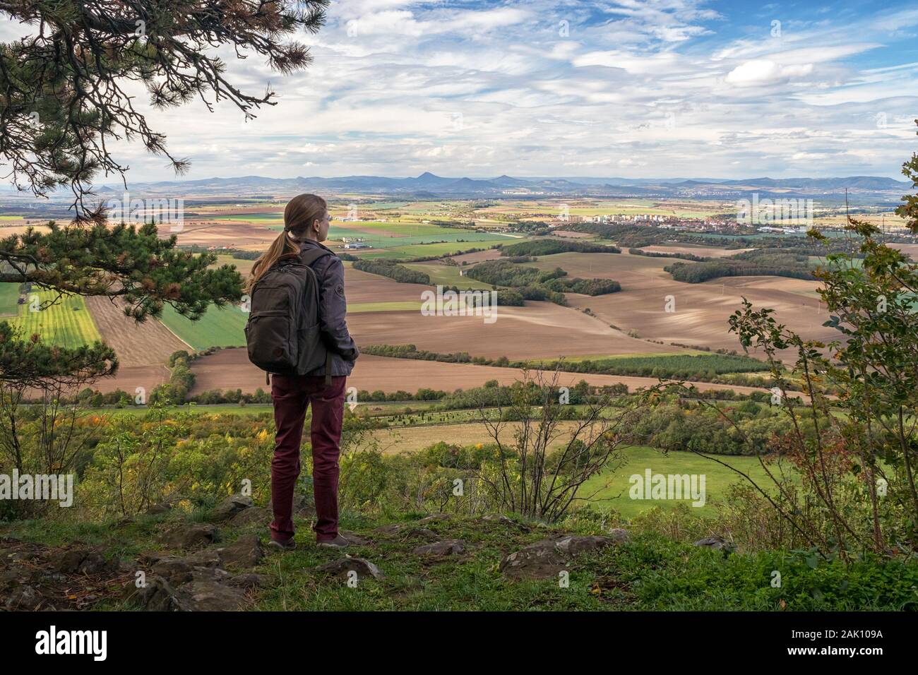 Giovane donna - escursionista che guarda il paesaggio rurale con villaggi, campi e montagne sullo sfondo, cielo blu con nuvole bianche, vista dal monte RIP, Foto Stock