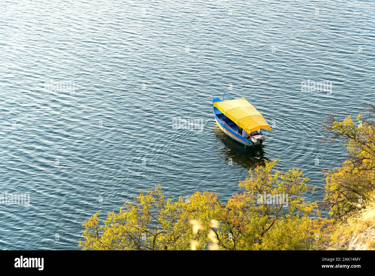 Blue imbarcazione turistica con giallo tetto in tela sul lago di Ohrid. Vista da sopra. Verdi alberi sulla riva del lago. Ohrid Macedonia nord, Europa. Foto Stock