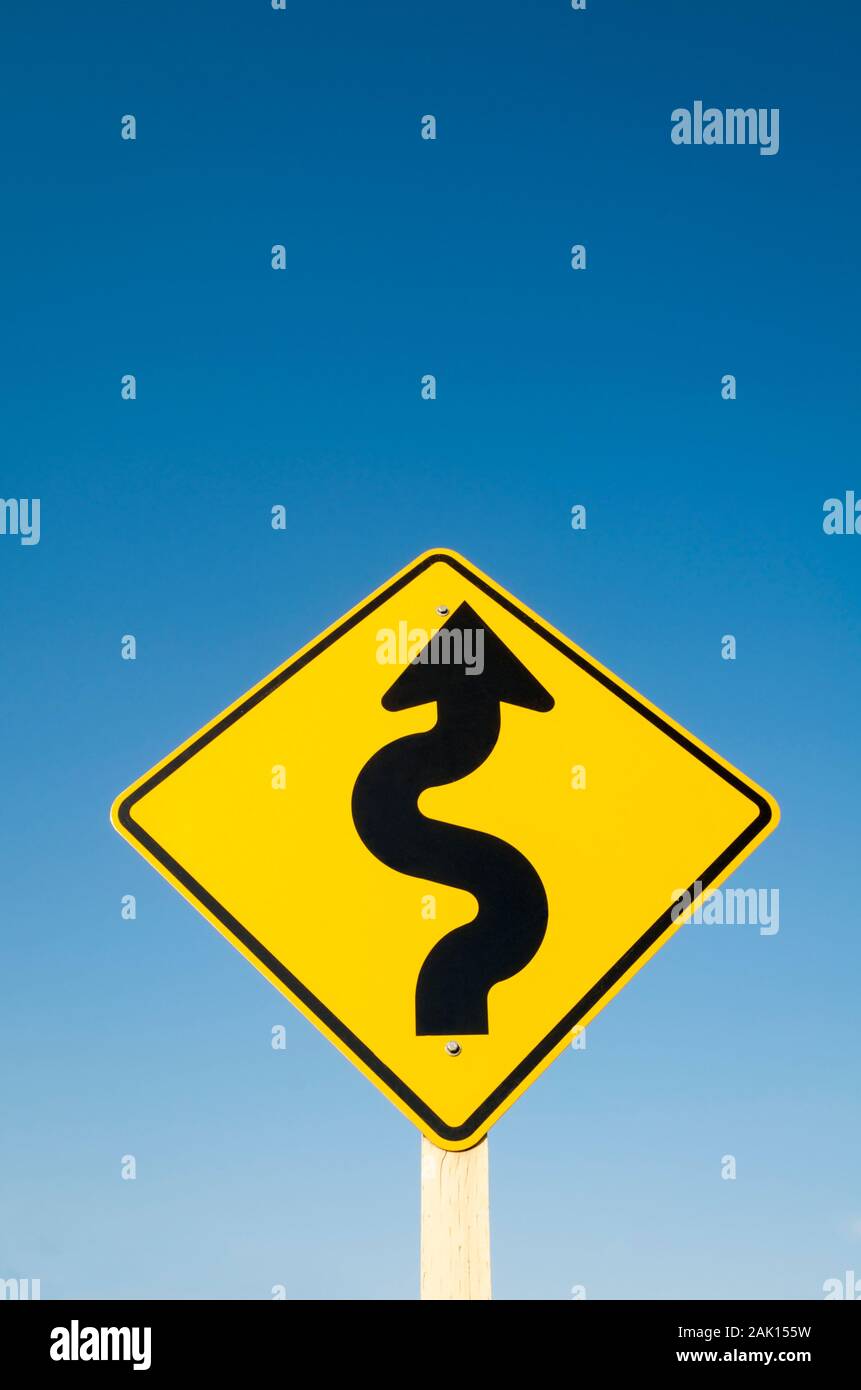Giallo cartello stradale con il nero della curvatura arrow attenzione di curve pericolose contro il cielo blu Foto Stock
