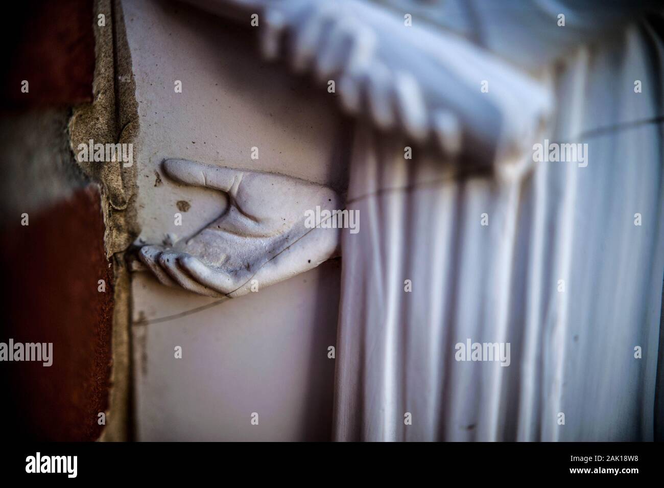 Una mano di pietra su una statua incrinato raggiunge fuori da dietro una figura umana Foto Stock